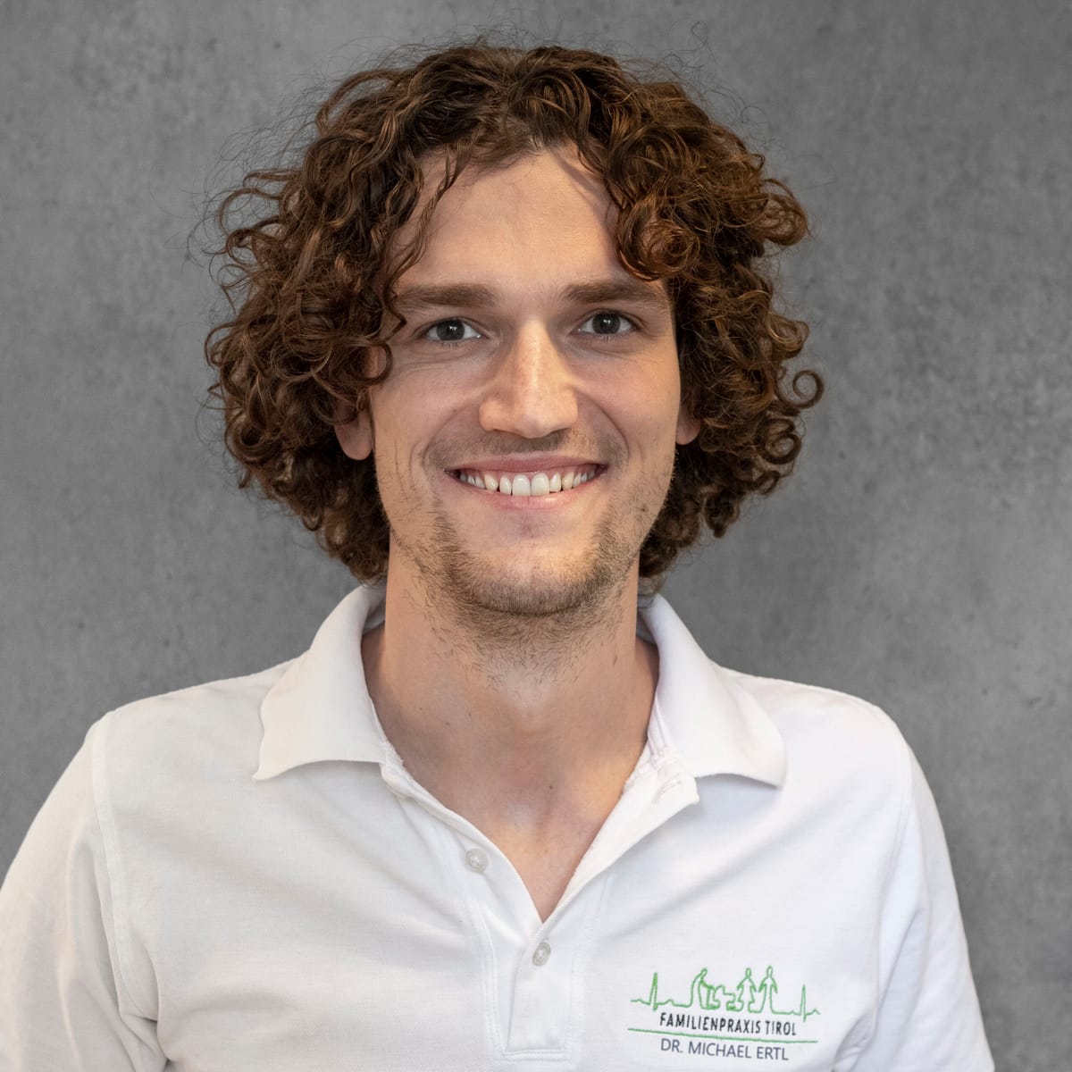 Dr Michael Ertl in white practice clothing against a grey background, looking friendly into the camera.